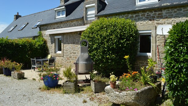 A stone house with a gravel driveway, a patio with outdoor furniture, and a garden with various plants and flowers. - Camélia de kerguével (Plonévez-Porzay)