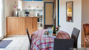 A dining area with a table set for two, a wooden counter, and a kitchen in the background. - Camélia de kerguével (Plonévez-Porzay)