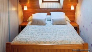 A small, cozy bedroom with a sloped ceiling and a skylight, featuring a bed with patterned bedding and two bedside lamps. - Camélia de kerguével (Plonévez-Porzay)