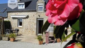 A stone house with a 'TOUT INCLUS' sign, outdoor seating, and potted plants. - Camélia de kerguével (Plonévez-Porzay)