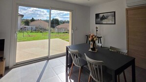 Un coin repas avec une table et des chaises, une porte-fenêtre coulissante donnant sur une terrasse, et un tableau encadré au mur.