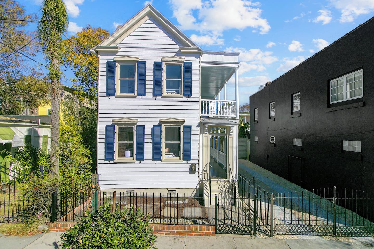 A two-story house with a balcony, a fenced yard, and a neighboring black building.