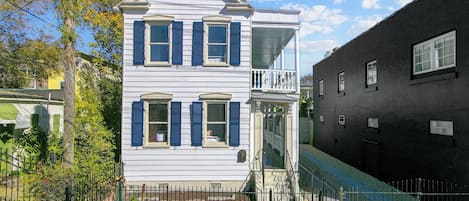 A two-story house with a balcony, a fenced yard, and a neighboring black building.
