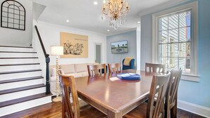 Een eetkamer met een houten tafel en stoelen, een kroonluchter en een trap met witte leuningen.