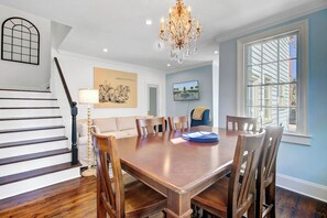Une salle à manger avec une table et des chaises en bois, un lustre et un escalier avec des rampes blanches.