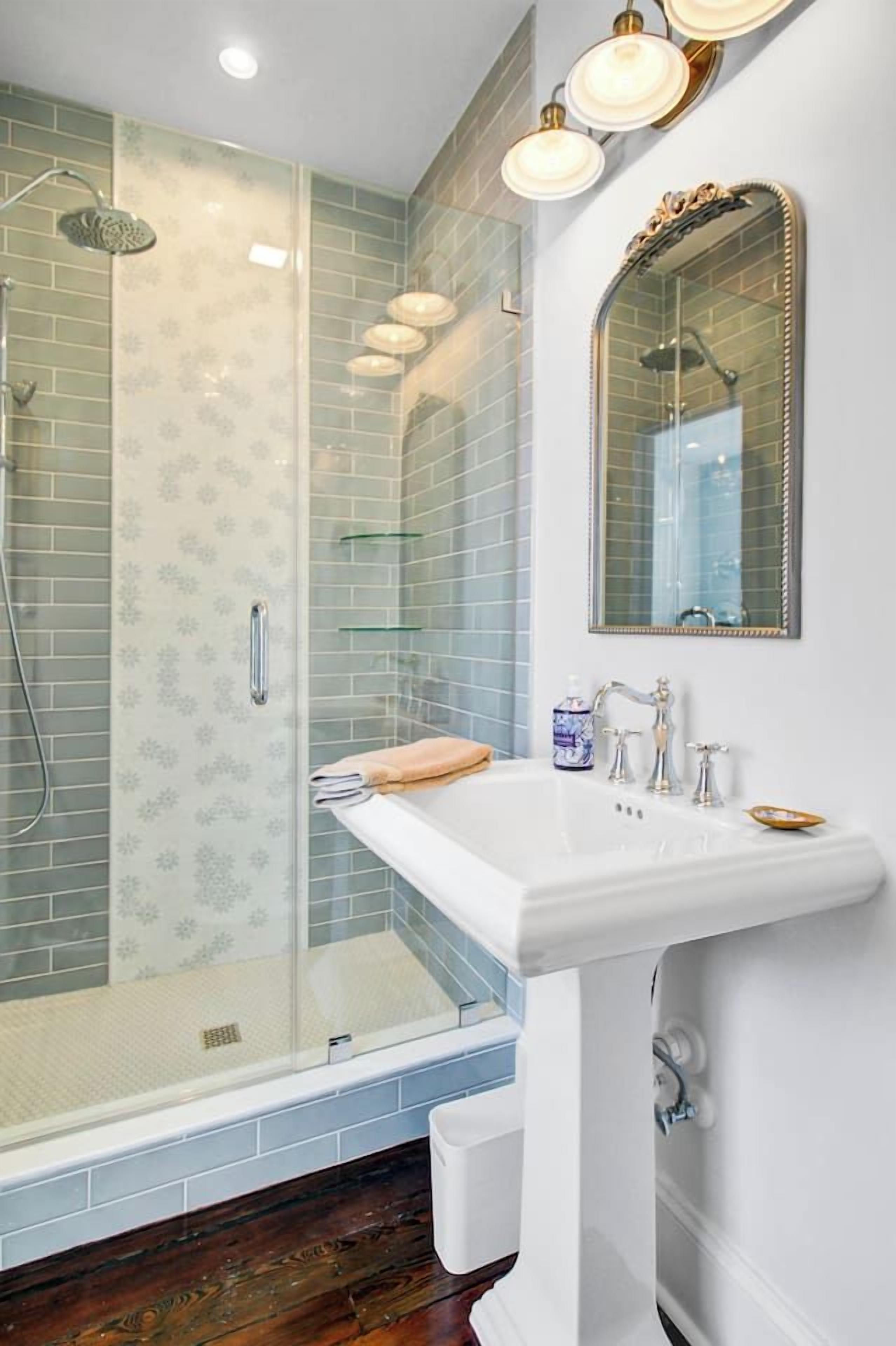 A bathroom with a glass shower enclosure, a white sink, and a mirror with an ornate frame.