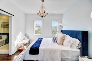 Une chambre à coucher avec un grand lit, un lustre, deux fenêtres et une vue sur l’extérieur.