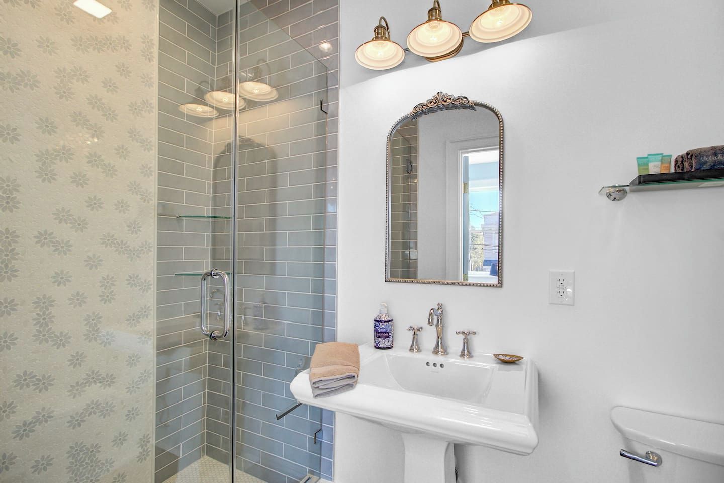 A bathroom with a glass shower enclosure, a white sink with a mirror, and a towel rack.