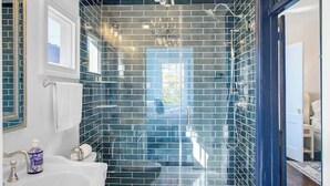 Een badkamer met een witte wastafel, een wit toilet, een douche met glazen cabine en een kroonluchter.
