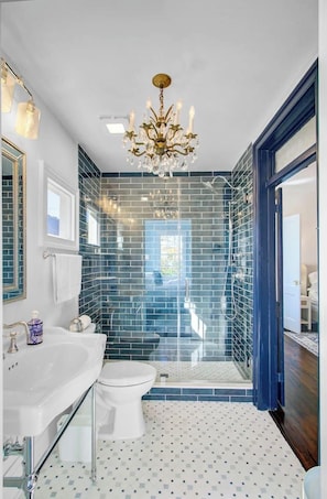 Une salle de bain avec un lavabo blanc, des toilettes blanches, une douche avec une paroi en verre et un lustre.