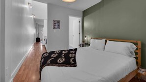 A bedroom with a wooden bed, white bedding, a patterned throw blanket, a bedside lamp, and a wall-mounted light fixture. - NEW WeHo Hotspot | 8 min Broadway, DTN + Music Row (Nashville)