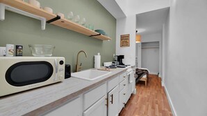 A compact kitchen with a microwave, sink, and wooden shelves. - NEW WeHo Hotspot | 8 min Broadway, DTN + Music Row (Nashville)