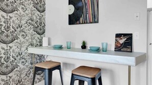 A modern kitchen with a white countertop, two stools, a decorative wall, and a framed picture. - NEW WeHo Hotspot | 8 min Broadway, DTN + Music Row (Nashville)