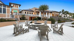 An outdoor seating area with Adirondack chairs and a circular fire pit, surrounded by a landscaped garden with palm trees and a stone wall. - Disney Home w/Private Pool - Resort Fun Sleeps 10 (Kissimmee)