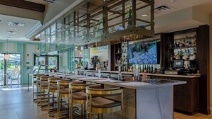 Zona de bar moderna con mostrador de mármol, taburetes y una pantalla de televisión mostrando un evento deportivo.