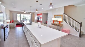Una cocina amplia con una isla grande, un comedor con un sofá rojo y una escalera con barandilla de madera.
