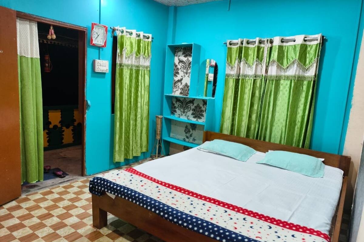 Un dormitorio con suelo a cuadros, una cama con colcha estampada, cortinas verdes y un reloj en la pared.