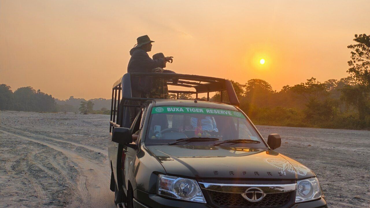 Um veículo estacionado em uma estrada de terra, com uma placa indicando "BUXA TIGER RESERVE".