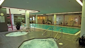 Une piscine intérieure dotée de plusieurs couloirs, un espace séparé avec un bain à remous et un coin salon agrémenté de sièges et de plantes.