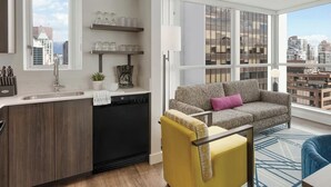 Un salon moderne avec un canapé, un fauteuil jaune et un fauteuil bleu, une machine à café et un téléviseur posé sur un meuble.