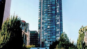 Un immeuble de grande hauteur doté d’une façade moderne en verre, entouré d’arbres et d’autres bâtiments.