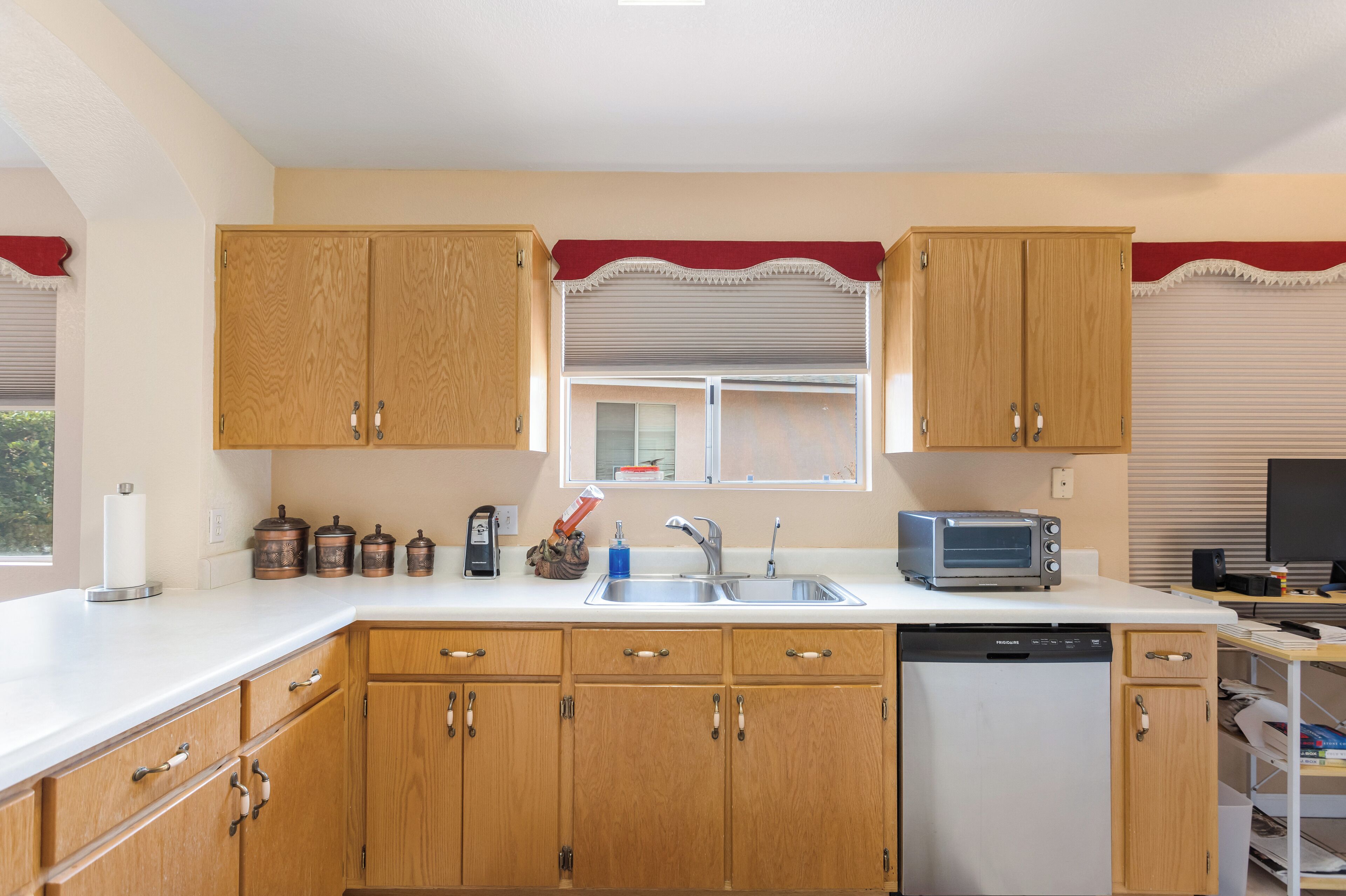 Una cocina con armarios de madera, lavavajillas, tostadora y ventana con persianas.