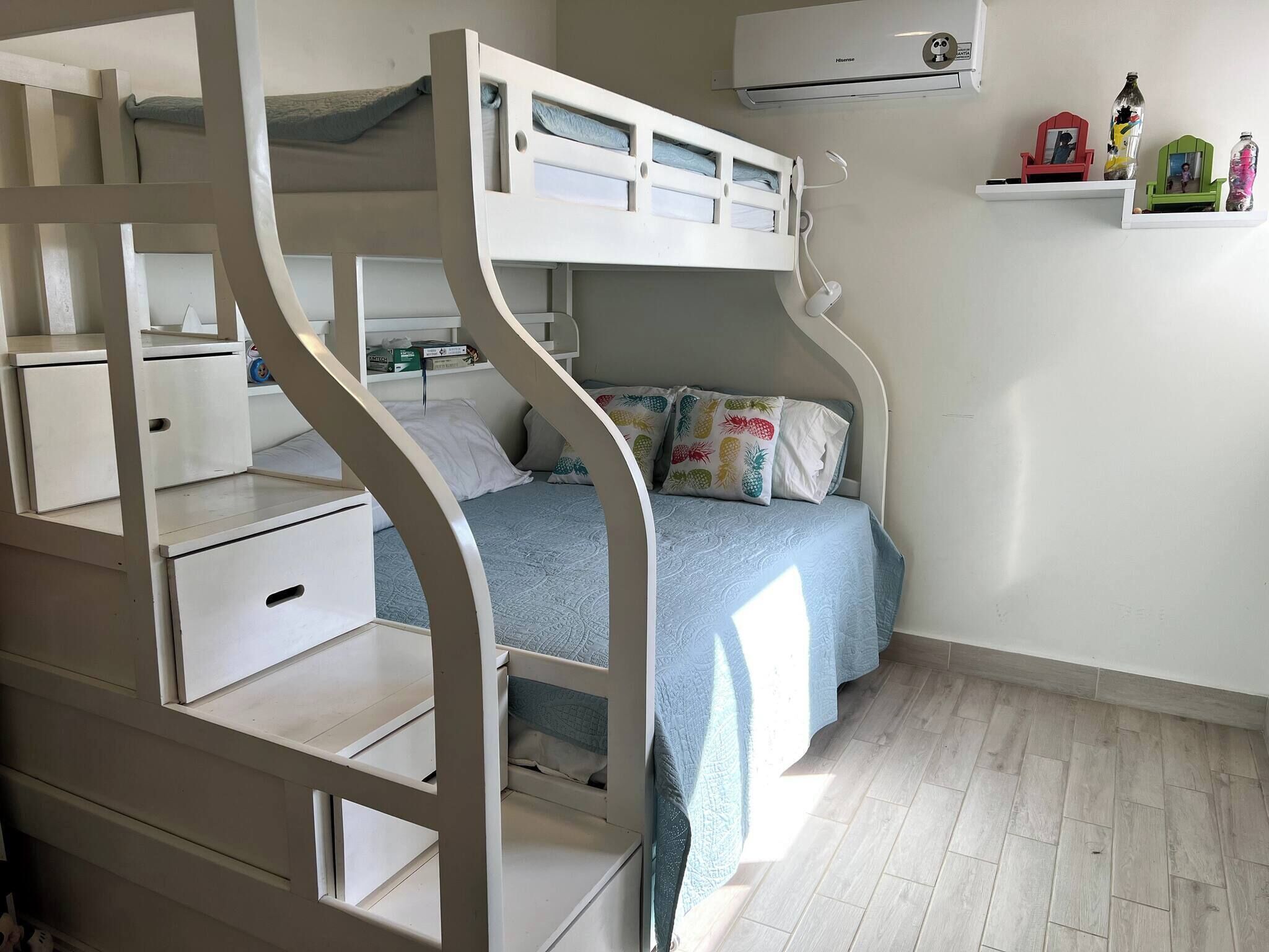 Habitación con literas, un escritorio y estanterías, aire acondicionado de pared y un pequeño estante con objetos decorativos.
