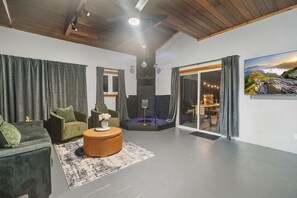 A modern living room with a sofa, armchair, and round coffee table. There is a glass door leading to a balcony with a view of a mountainous landscape. - Near Ithaca| Hot Tub | Karaoke Room | Dogs Okay (Newfield)