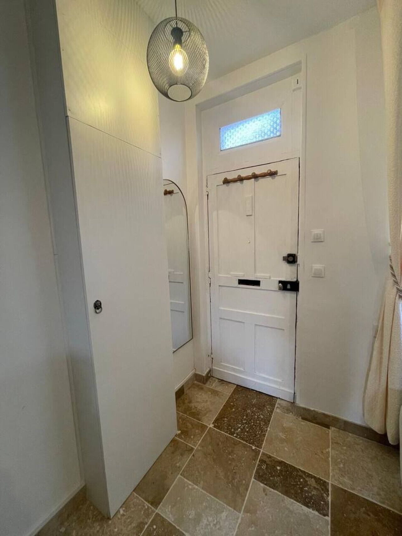 Un couloir avec une porte blanche, un miroir et un luminaire suspendu.