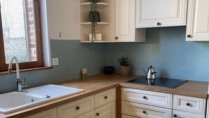 A kitchen with white cabinets, a sink, a window, and a potted plant on a shelf. - Le confort avec jardin, à deux pas du port (Fécamp)