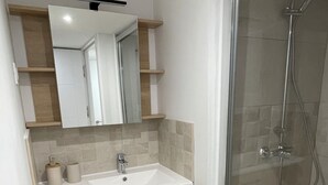 A modern bathroom with a glass shower enclosure, a white sink, and wooden cabinetry. - Town house, 4 bedrooms / 4 bathrooms, large living room and terrace (CARCASSONNE)