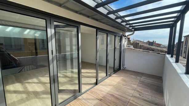 A balcony with a wooden floor and glass doors leading to an interior space. - Town house, 4 bedrooms / 4 bathrooms, large living room and terrace (CARCASSONNE)