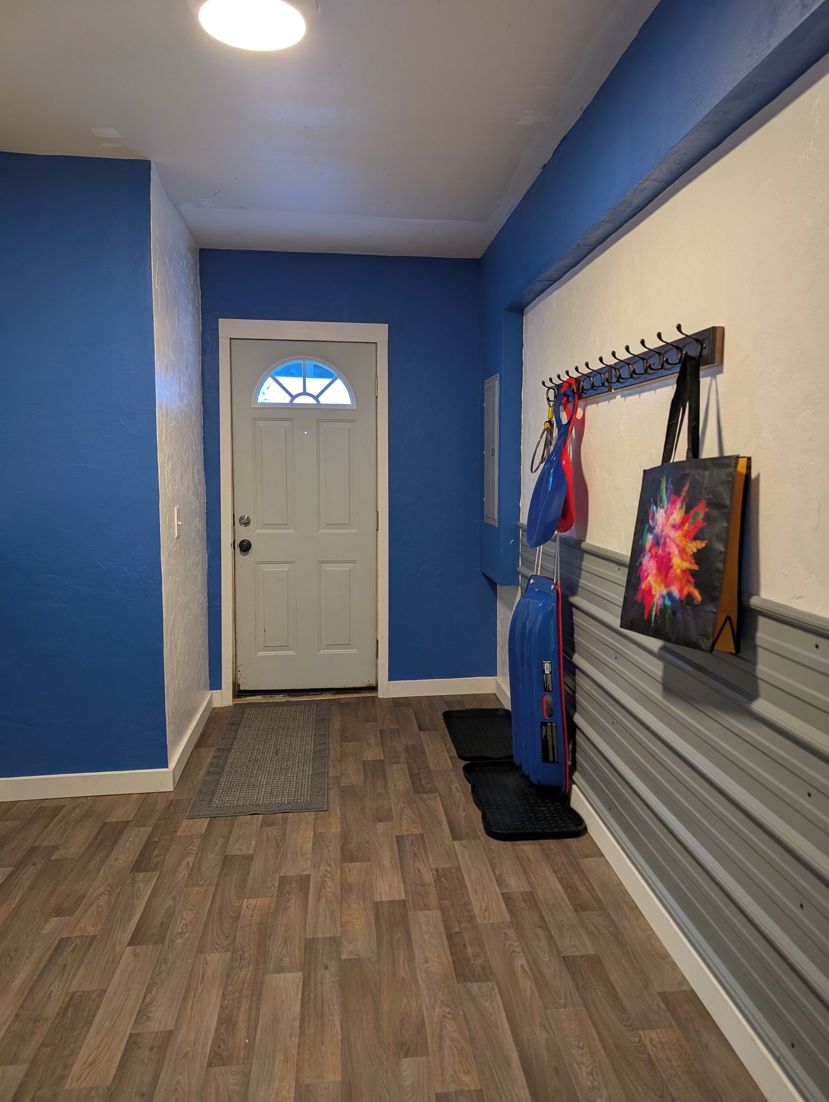 A hallway with blue walls, a white door, and a coat rack with a bicycle and a painting.