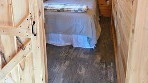Una habitación de cabaña de madera con una cama, un cuadro de un oso en la pared y una ventana con cortinas.