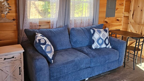 Interior acogedor de una cabaña con un sofá azul, una mesita y un techo rústico de madera.