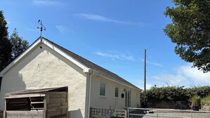 A single-story building with a sloped roof, a wooden garage door, and a metal gate. - Swallow Bach, Couples Bolt Hole (Llangefni)