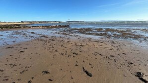 A beach with a pier extending into the water, sandy shore, and distant mountains. - Swallow Bach, Couples Bolt Hole (Llangefni)