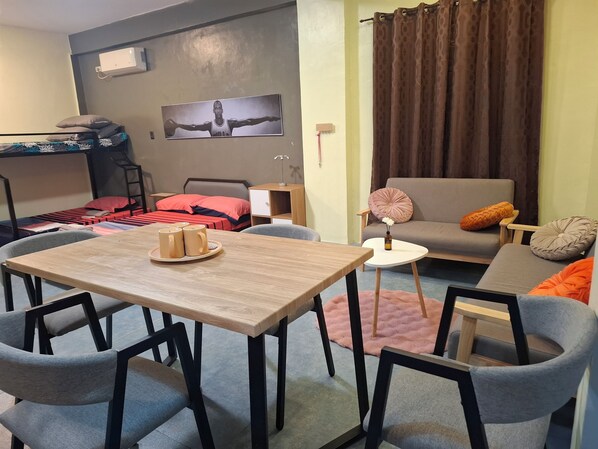 Ein modernes Wohnzimmer mit einer Couch, einem Esstisch mit Stühlen, einem Stockbett und einer Wand-Klimaanlage.