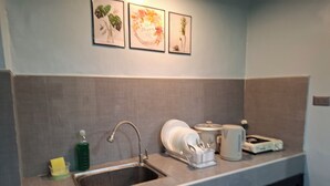 Una cocina con un lavamanos de acero inoxidable, un escurreplatos, una tetera y un tostador. Hay tres cuadros enmarcados en la pared sobre el lavamanos.