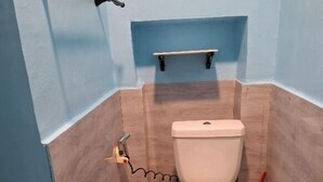 Un baño con inodoro, secador de manos y un estante sobre el inodoro.