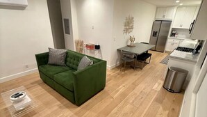 Een modern appartement met een groene bank, een eethoek, een keuken met een fornuis, en een prullenbak.
