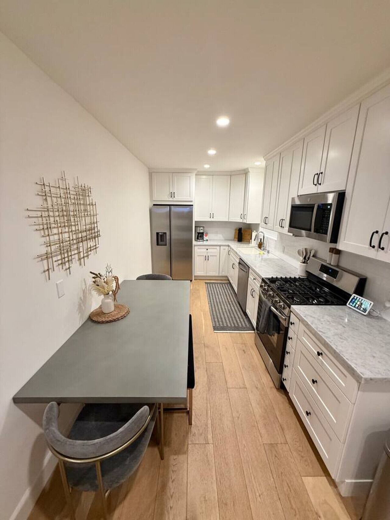 A modern kitchen with white cabinets, a stainless steel refrigerator, a microwave, and a gas stove.