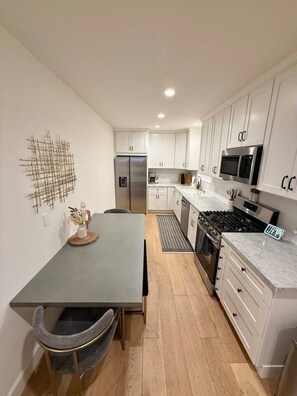A modern kitchen with white cabinets, a stainless steel refrigerator, a microwave, and a gas stove.
