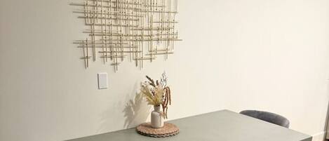 A dining area with a grey table, two chairs, a bench, and a wall-mounted abstract art piece.