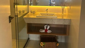 Een moderne badkamer met een glazen douchecabine, een granieten aanrechtblad, een wastafel met spiegel erboven en een decoratieve handdoekenopstelling.