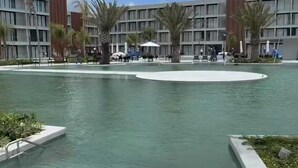 Een modern hotel met een centraal gelegen zwembad, omringd door palmbomen en een heldere lucht.