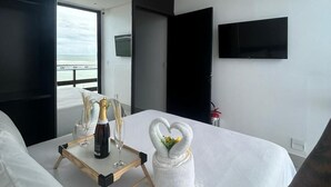 Een moderne hotelkamer met een bed, een nachtkastje met een fles champagne, een glas en een decoratieve zwaan van handdoek.