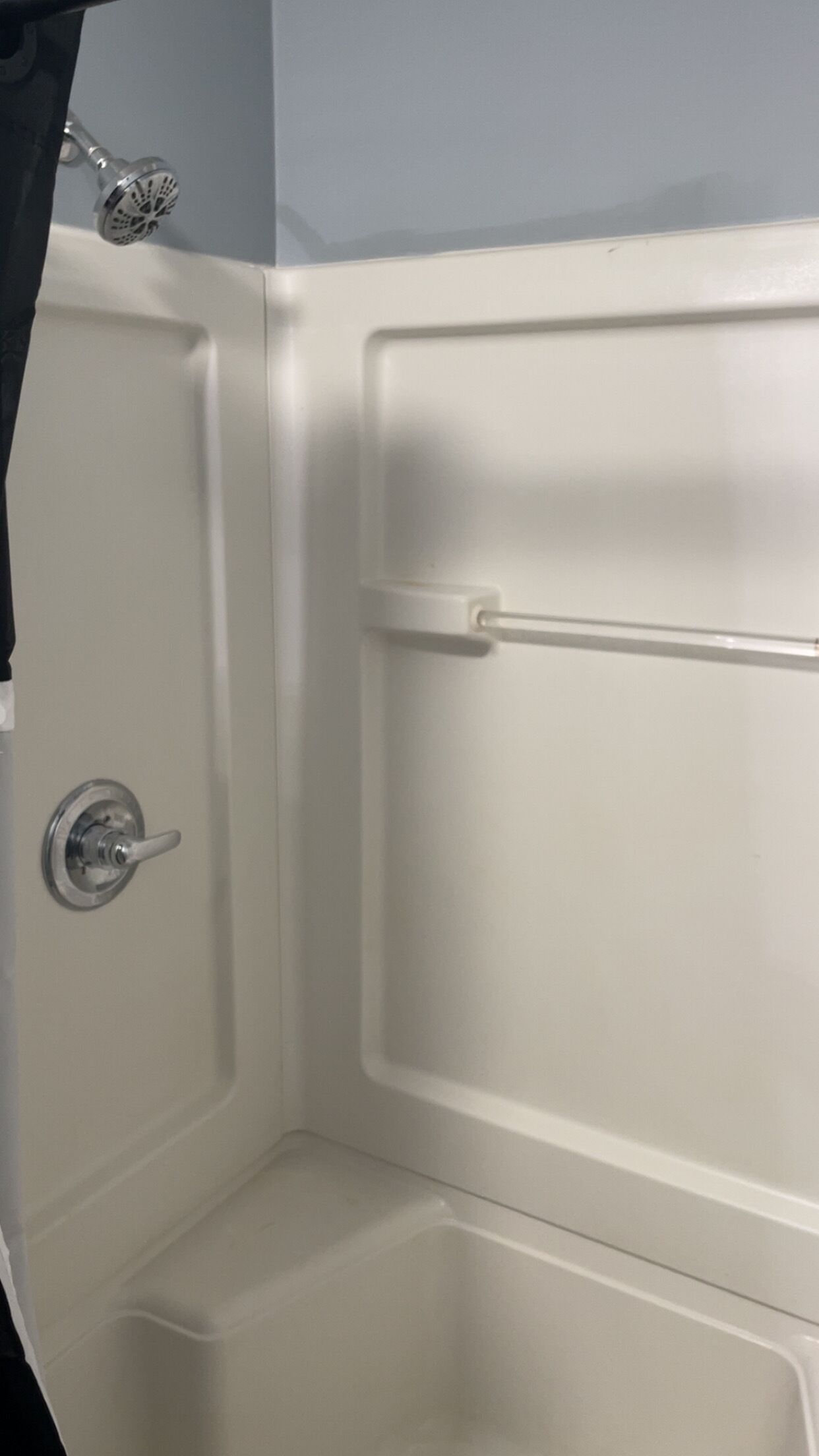 A white shower enclosure with a handheld showerhead and a control knob.