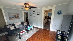 A living room with a sofa, coffee table, and a ceiling fan. There is a kitchen visible through an open doorway. - Cozy 2-bedroom house in beautiful Andrews,NC with theater room and air hockey. (Andrews)
