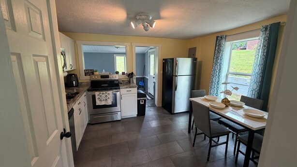 A compact kitchen with a refrigerator, oven, and microwave. There is a dining area with a table and chairs. - Cozy 2-bedroom house in beautiful Andrews,NC with theater room and air hockey. (Andrews)